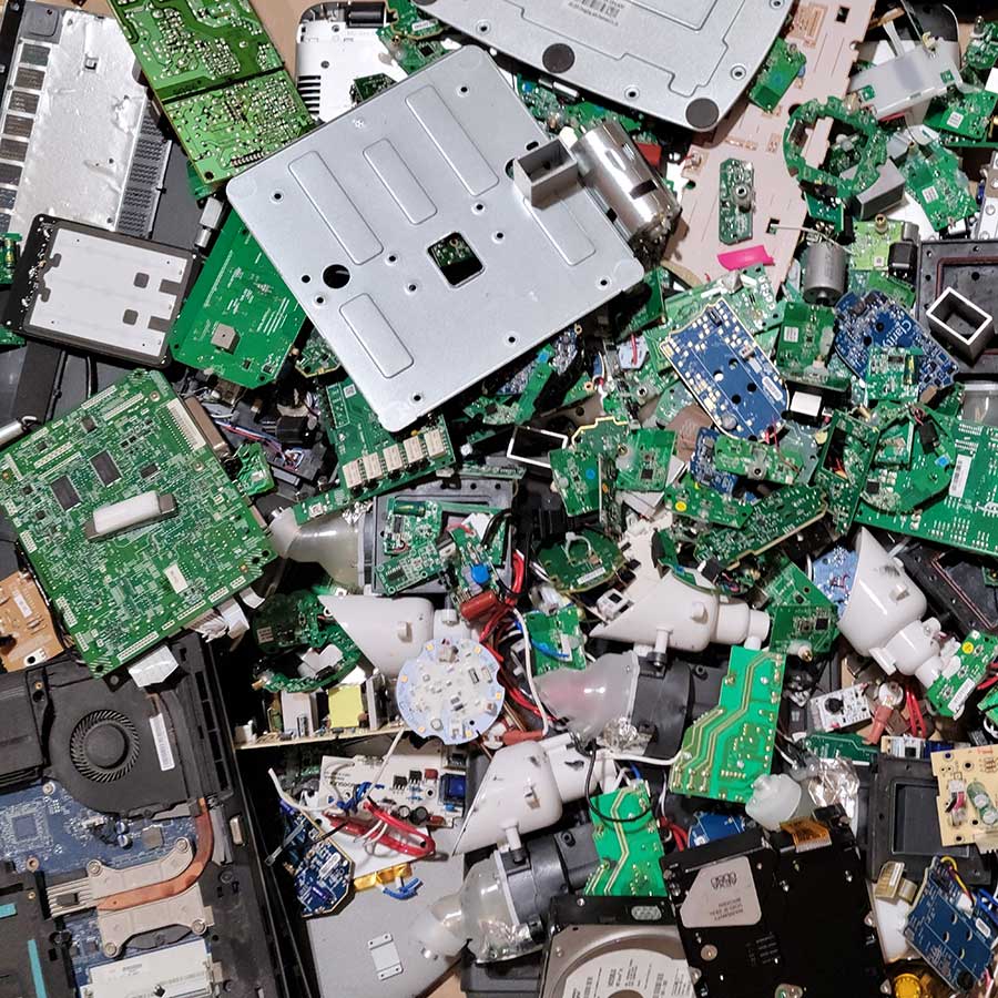 A pile of assorted electronic waste, including circuit boards, wires, metal components, and plastic parts, scattered closely together and creating a colorful, chaotic jumble.