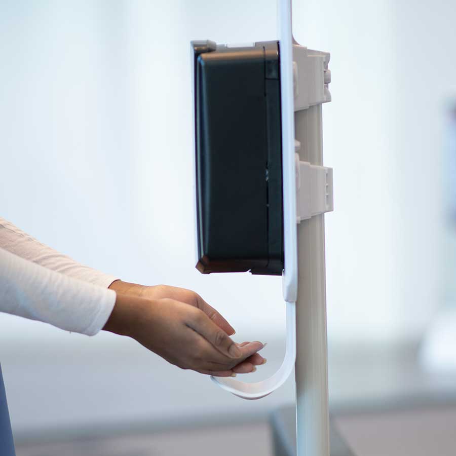 A person holds their hands under a wall-mounted automatic hand sanitizer dispenser, allowing sanitizer to drip onto their palm.