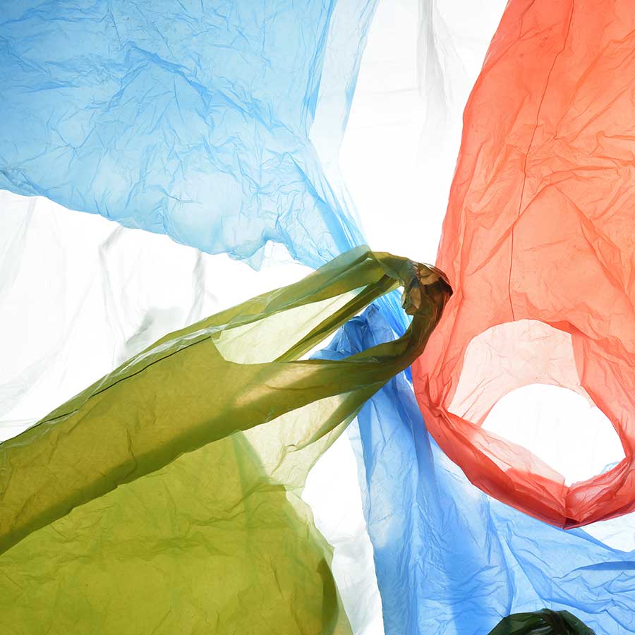 Translucent plastic bags in blue, red, and green overlap and float against a bright white background, creating abstract shapes and soft, crinkled textures.