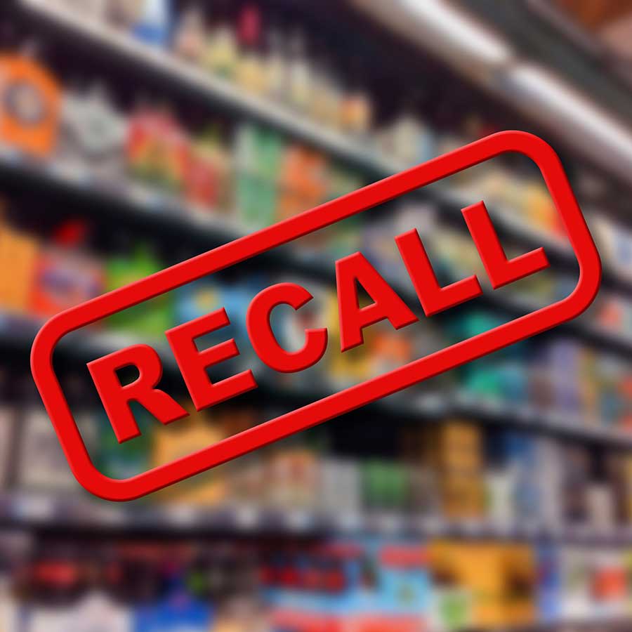 A red RECALL stamp is prominently displayed over blurred shelves of assorted grocery products in a store.